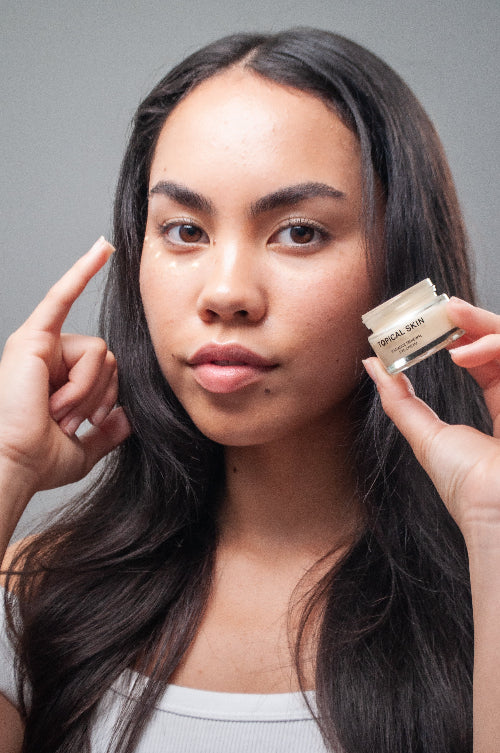 Woman holding a jar of skincare product against a neutral background