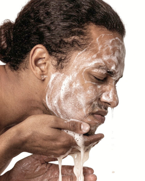 Person washing their face with a white substance against a white background