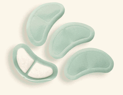 Four pale mint green silicone or foam pads with irregular curved shapes, including one pad shown from the inside with white textured inserts, arranged on a light cream background.