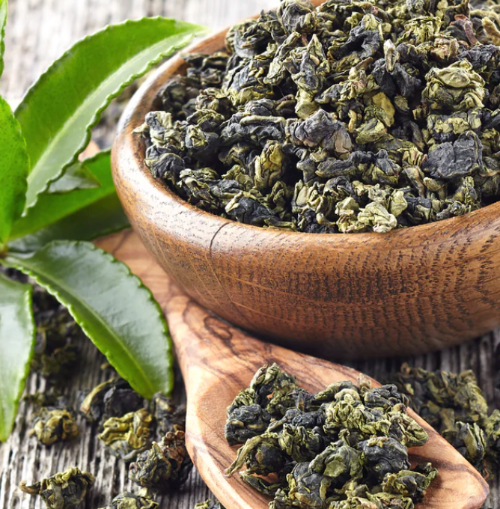 Wooden bowl and spoon filled with green tea leaves on a wooden surface