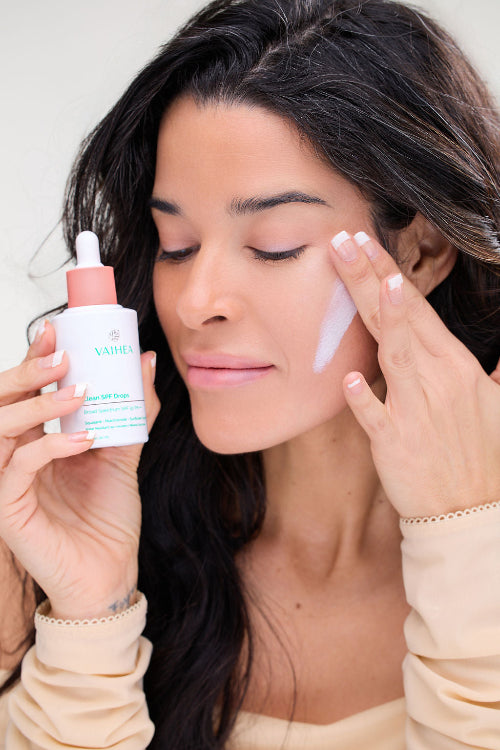 Woman applying skincare product to her face with a dropper bottle in hand.