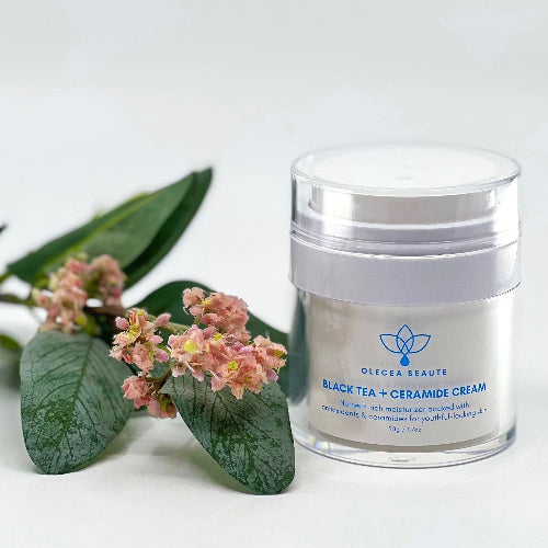 Jar of Oleaera Beaute Black Tea + Ceramide Cream with flowers and leaves on a light background