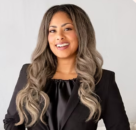 Woman with long, wavy hair smiling against a plain background