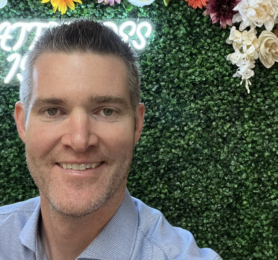 Brian Watson in front of a green wall with flowers and neon signs