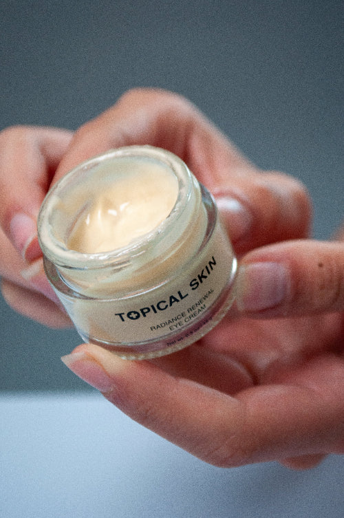 Hand holding a jar of 'Topical Skin' eye cream against a neutral background