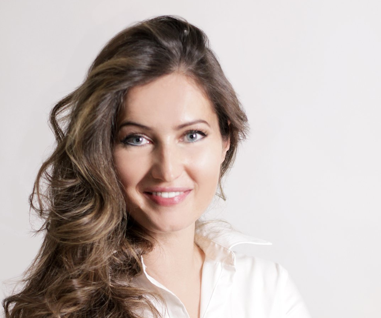 Woman with long, wavy hair smiling against a plain background