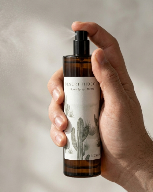 Hand holding a bottle of 'Desert Hideout' room spray with cactus design on label.