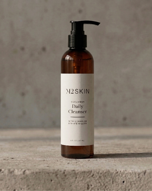 Brown bottle of M2SKIN Daily Cleanser on a concrete surface with a neutral background
