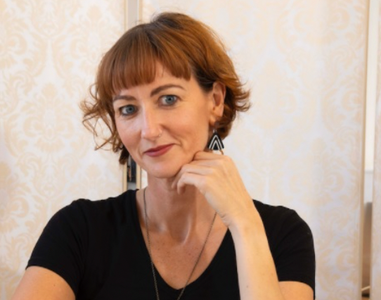 Niamh with short brown hair and a black top against a light patterned wall.