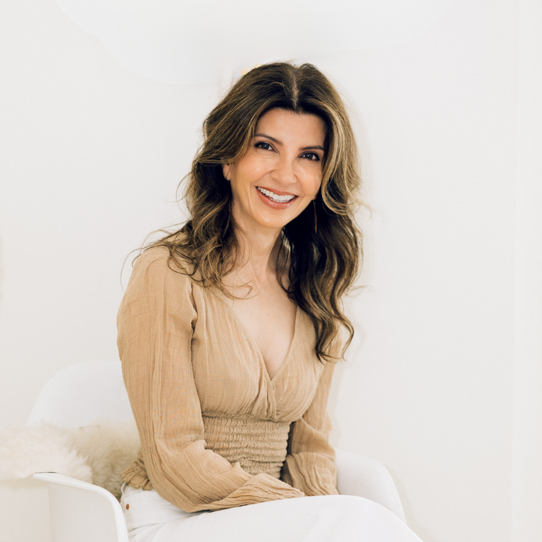 Raana in a beige dress sitting on a white couch.