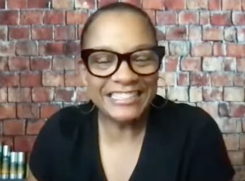 Person wearing glasses smiling in front of a brick wall.