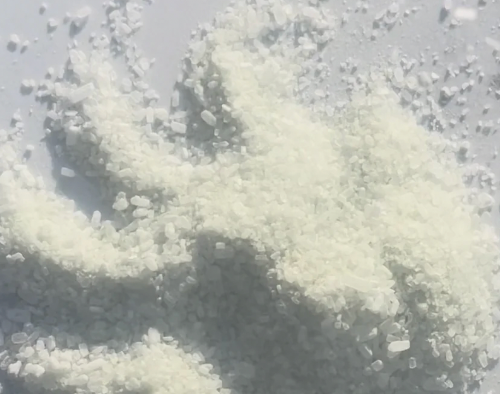 A close-up of a pile of fine white crystalline powder or salt grains on a light gray surface.