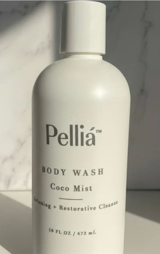 A white bottle of Pellía Body Wash Coco Mist, featuring a minimalist white label with black text, set against a light gray marble background with soft diagonal shadows.