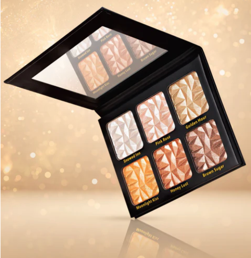 An open six-pan makeup highlighter palette with a black case, displayed at an angle against a warm, sparkling gold background. The pans feature shimmering highlighters in shades of champagne, rose gold, honey, and brown, with labels reading 'Champagne', 'Pink Rose', 'Golden Hour', 'Moonlight Kiss', 'Honey Lust', and 'Brown Sugar'.