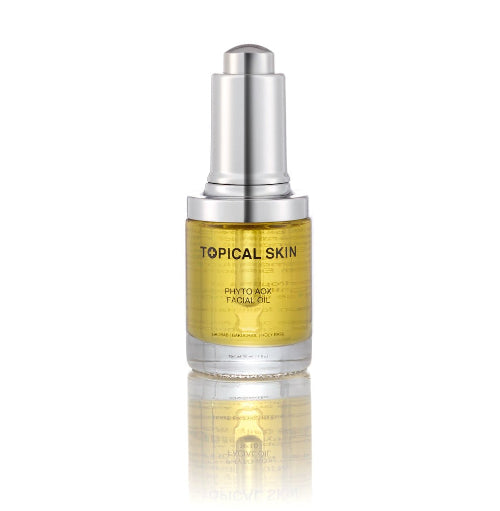 A bottle of TOPICAL SKIN Photo-Awaken Facial Oil with a silver pump and a clear glass body showing golden-yellow oil inside, set against a plain white background with a soft reflection below.