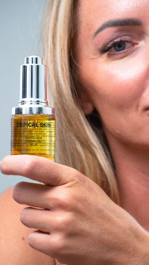 Person holding a bottle of 'Topical Skin' serum close to their face.