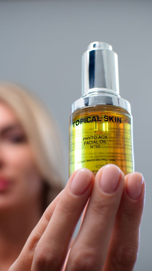 Bottle of 'Topical Skin' facial oil held by a hand with a blurred background